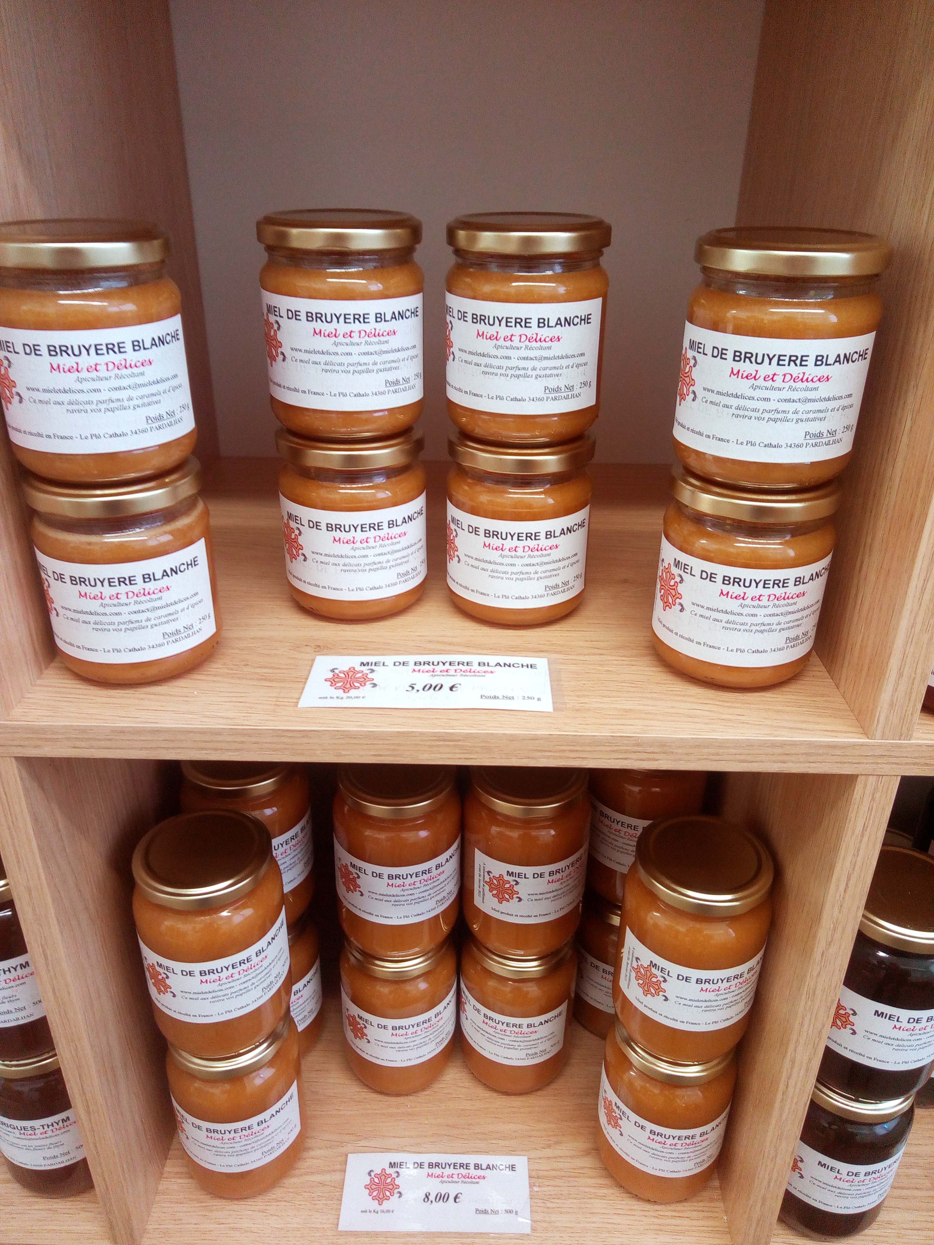 Photo d'un rayon bien garni de la boutique Miel et Délices, présentant une variété de pots de miel aux textures et couleurs différentes (miels liquides, crémeux, clairs, foncés). L'image met en valeur l'abondance et la diversité des miels artisanaux proposés directement par l'apiculteur.