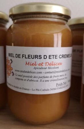 Pot de miel de fleurs d'été crémeux Miel et Délices, montrant sa texture onctueuse et sa couleur claire. Ce miel doux aux notes florales est idéal pour les tartines, récolté artisanalement en Hérault.
