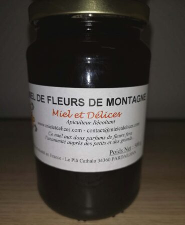 Pot de miel de fleurs de montagne Miel et Délices, montrant sa couleur claire et sa texture veloutée. Ce miel pur et délicat, aux arômes floraux variés, est récolté artisanalement en montagne.